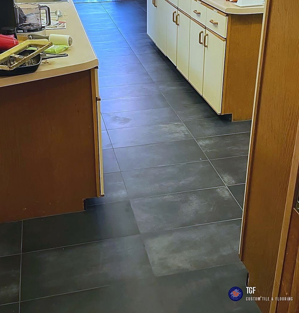 The same kitchen after — large-format charcoal porcelain tile replacing the carpet