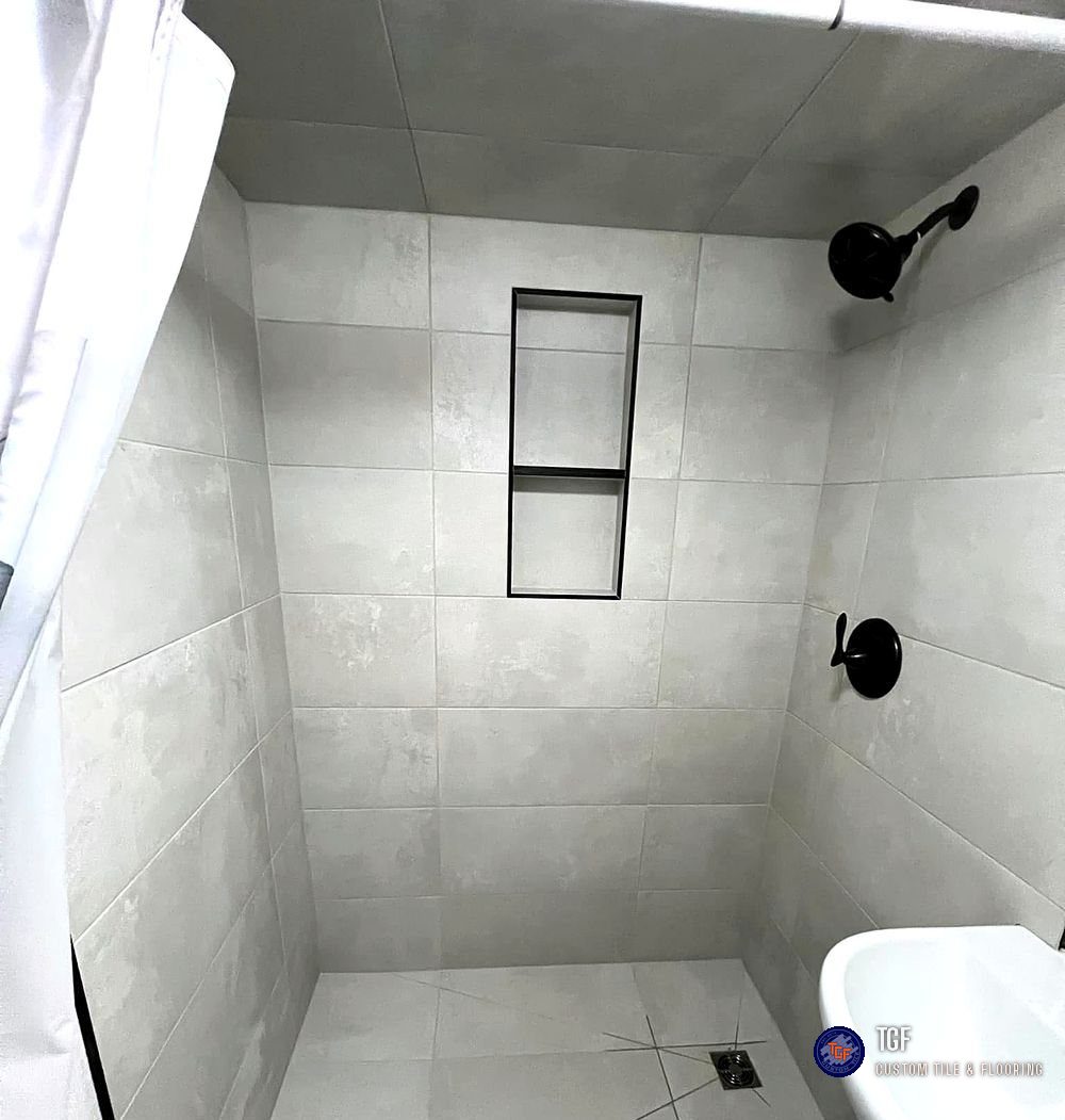 The same bathroom after — a fully tiled walk-in shower with black fixtures and a built-in niche