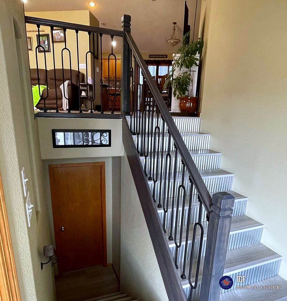 The same staircase after — porcelain tile treads, fluted risers, and a stained railing with wrought-iron balusters