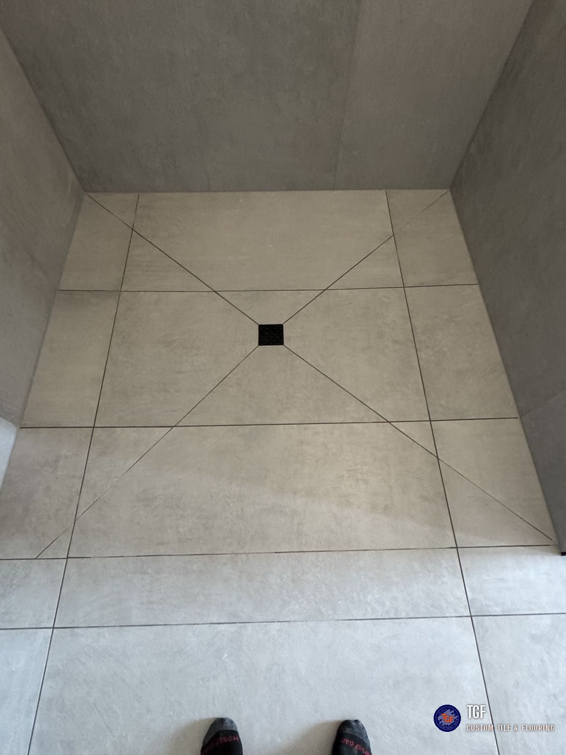 A curbless shower floor in large-format tile, cut to a four-way pitch to the center drain
